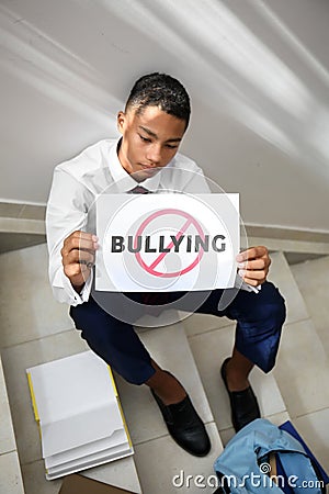 African-American teenage boy holding sheet of paper with word BULLYING at school Stock Photo
