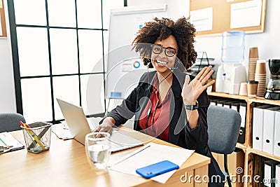 African american woman with afro hair working at the office wearing operator headset waiving saying hello happy and smiling, Stock Photo