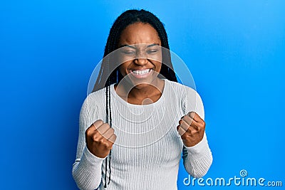 African american woman with braided hair wearing casual white sweater very happy and excited doing winner gesture with arms Stock Photo