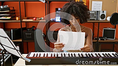 African american woman musician playing piano reading music sheet at music studio Stock Photo