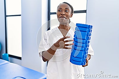 African american woman physiotherapist smiling confident holding foam roller at rehab clinic Stock Photo