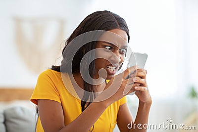 African American woman receiving bad news, angry at her smartphone at home Stock Photo