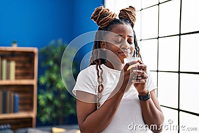 African american woman smelling aromatic candle standing at home Stock Photo