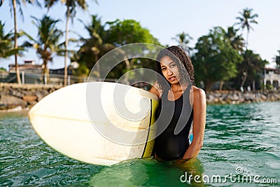 African american woman standing with surfboard in ocean water. Black female surfer posing with surf board. Pretty Stock Photo