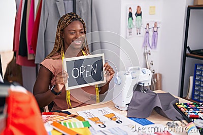 African american woman tailor sitting on table holding open blackboard message at tailor shop Stock Photo