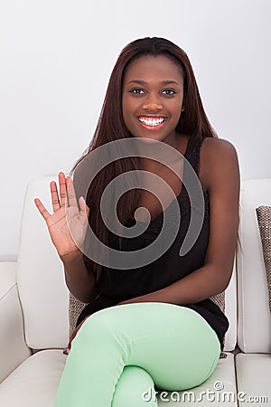 African American woman waving while sitting on sofa Stock Photo