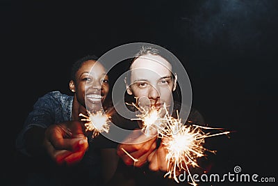 African American woman and a Caucasian man couple playing with sparklers celebration and festive party concept Stock Photo