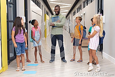 African american young male teacher talking to multiracial elementary students standing in corridor Stock Photo