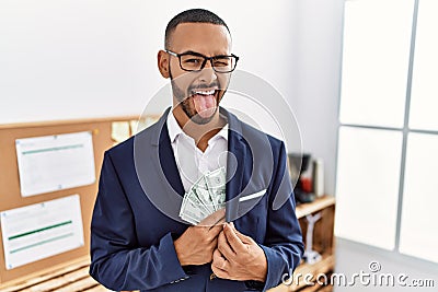 African american young man hiding dollars in jacket sticking tongue out happy with funny expression Stock Photo