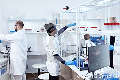 African in biotechnology laboratory reaching for glass flask Stock Photo