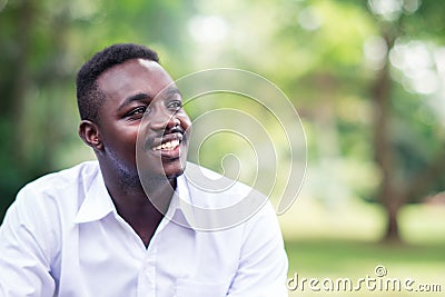 African business man in white shirt smiling and sitting outside with green trees on background Stock Photo