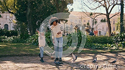 African child feeding birds with mother in park. Girl throwing food to pigeons. Stock Photo