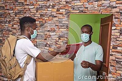 African client wearing a medical mask receiving a parcel from a young African courier Stock Photo