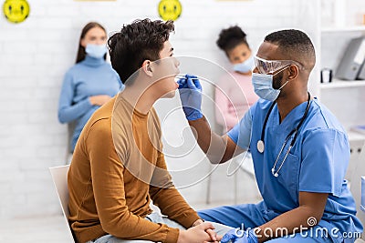 African Doctor Testing Asian Patient For Coronavirus Sitting In Clinic Stock Photo