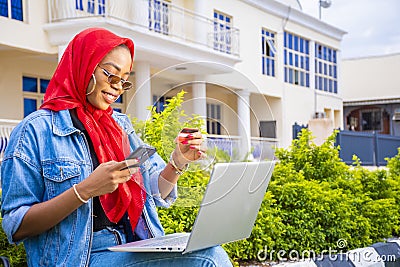 African female sitting outside with her laptop and phone making a payment online Stock Photo