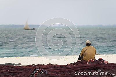 African fisherman sitting on fishing nets looks out to sea Editorial Stock Photo