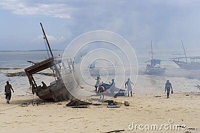 African fishermen set fire under their traditional wooden Dhow boat on the beach to protect it from pests and woodworm and repair Editorial Stock Photo