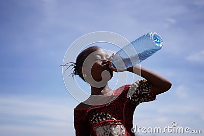 African Girl Drinking From a Water Bottle Under An Intensely Blue Sky Stock Photo