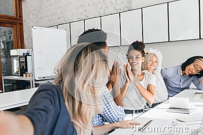 African girl in t-shirt playing with colleague in funny game in office. Attractive young female worker fooling around Stock Photo