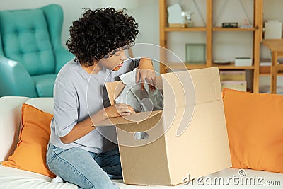 African girl unpacking delivery looking in box. Happy woman opening carton box. Female getting parcel looking at Stock Photo
