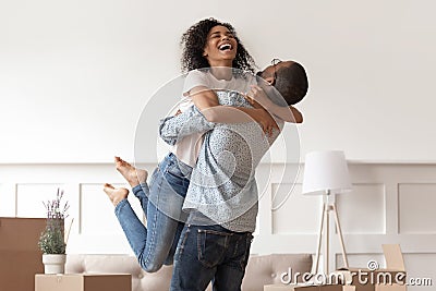 African husband lifting happy wife celebrating moving day with boxes Stock Photo