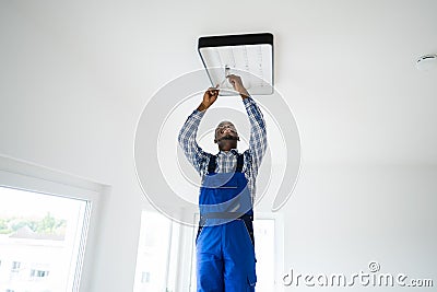 African Maintenance Electrician On Ladder Fixing Stock Photo