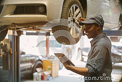 African maintenance male checking tire service via insurance system at garage with using tablet Stock Photo