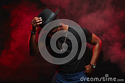 African male dancer with hat dancing in black t-shirt in dark red smoky club Stock Photo