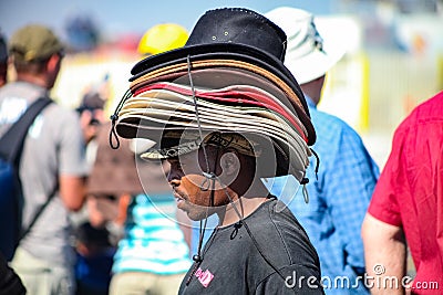 African man hawker wearing a pile of hats on his head at outdoor event Editorial Stock Photo