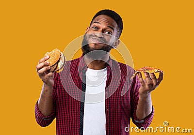 African Man Holding Burger And Slice Of Pizza, Yellow Background Stock Photo