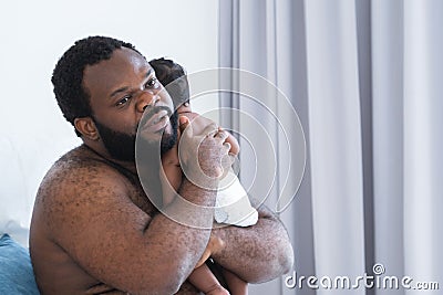 African middle aged bearded father is soothing newborn baby crying in his arms and shoulder in bedroom at home. Single dad hugging Stock Photo