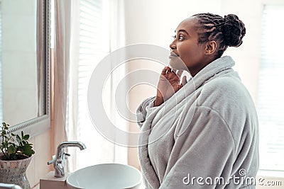 African woman looking at her complexion in a bathroom mirror Stock Photo