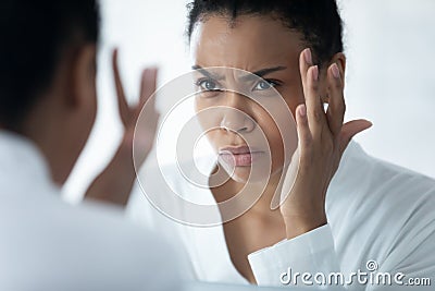 African woman looking in mirror see mimic wrinkles feels stressed Stock Photo