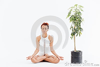 African woman meditating in lotus pose near tree in pot Stock Photo