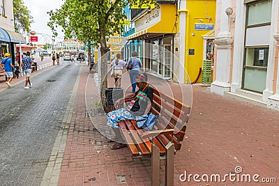 An African woman peacefully napping on a bench surrounded by people and tourists strolling through Willemstad's Editorial Stock Photo