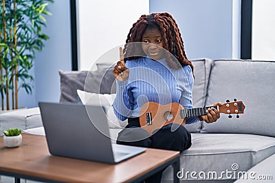 African woman playing ukulele at home doing video call smiling with an idea or question pointing finger with happy face, number Stock Photo