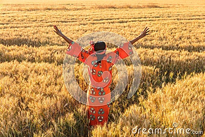 African woman in traditional clothes arms raised in field of crops at sunset or sunrise Stock Photo