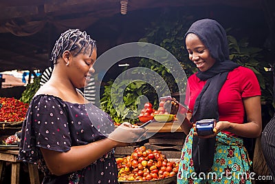 African woman shopping food stuff in a local market paying by doing mobile transfer via phone for a trader Stock Photo