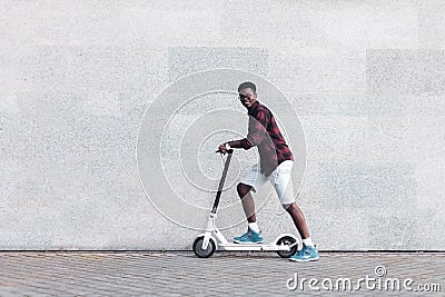 Afro american guy rides an electric scooter against the background of a wall, student uses eco transport Stock Photo