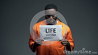 Afro-american imprisoned male holding life sentence sign, looking to camera Stock Photo
