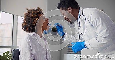 Afro-american male doctor examining young woman throat in office. Stock Photo