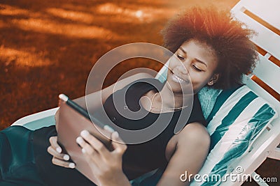 Afro girl laying on a daybed with digital tablet Stock Photo