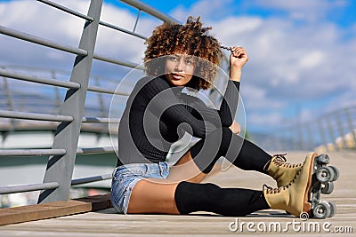 Afro hairstyle woman on roller skates sitting on urban bridge Stock Photo