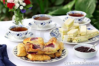 Afternoon tea in the garden with scones, strawberry jam, finger sandwiches with cucumber and egg salad. Stock Photo