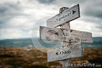 Against all odds text on wooden rustic signpost outdoors in nature/mountain scenery. Stock Photo