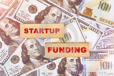 Against the background of dollar bills, the text is written on wooden blocks - startup funding Stock Photo