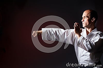 Against a dark red background, a young athlete makes a punch and block with his hand Stock Photo