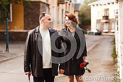 Age couple in leather coats walking through the city streets in the summer. Happy man and woman forty five years old Stock Photo