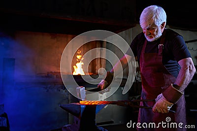 Aged blacksmith forged iron on anvil using heavy hammer Stock Photo