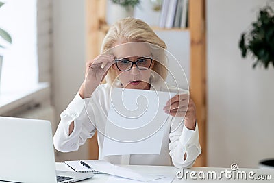 Middle-aged businesswoman lowered glasses reading letter feels shocked Stock Photo